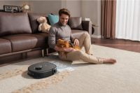 Man with dog sitting by Eufy X10 Pro Omni cleaning carpet