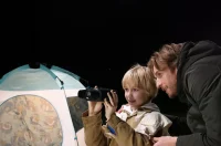 Adult and child observing through AKASO Seemor at night near a tent.