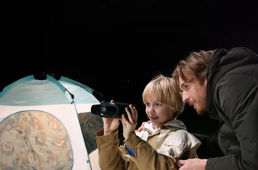 Adult and child observing through AKASO Seemor at night near a tent.
