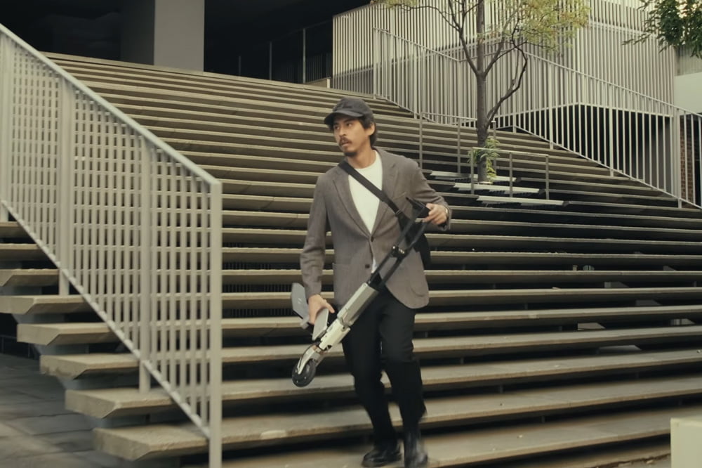 Man carrying folded Arma Scooter on stairs.