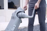 Person holding Unitree Go2 robot by the leg on a paved surface