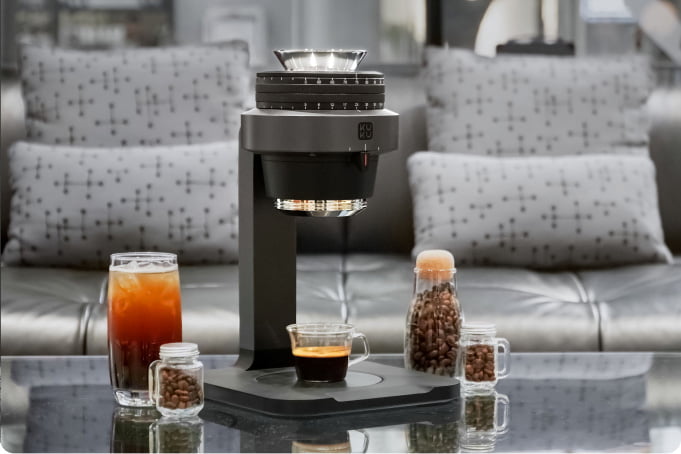 KUKU Maker on a glass table with coffee and coffee beans around it.