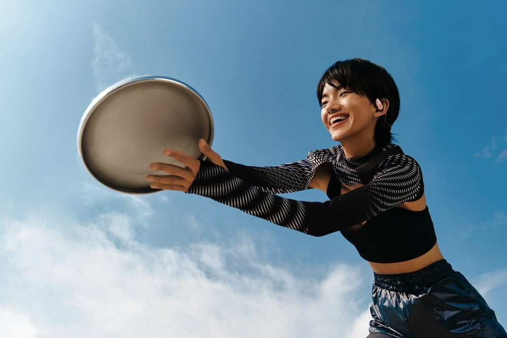 Woman smiling while catching a disc, wearing OWS Sports earphones