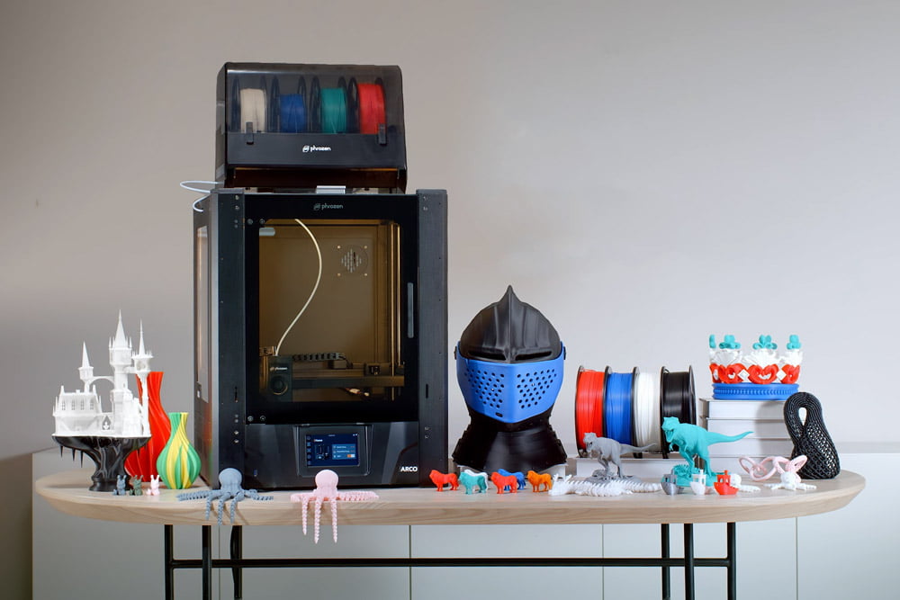 Wider shot of Phrozen Arco 3D printer with various printed objects and filament spools