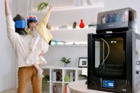 Adult lifting a child wearing a 3D printed crown, with Phrozen Arco printer in background.