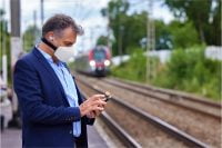 Man checking his phone with a Skyted mask at a train station.