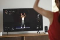 Woman lifting dumbbells in front of a Tempo Studio screen