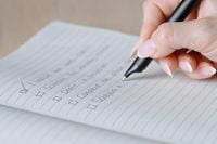 Close-up of a hand writing checkmarks in a lined notebook