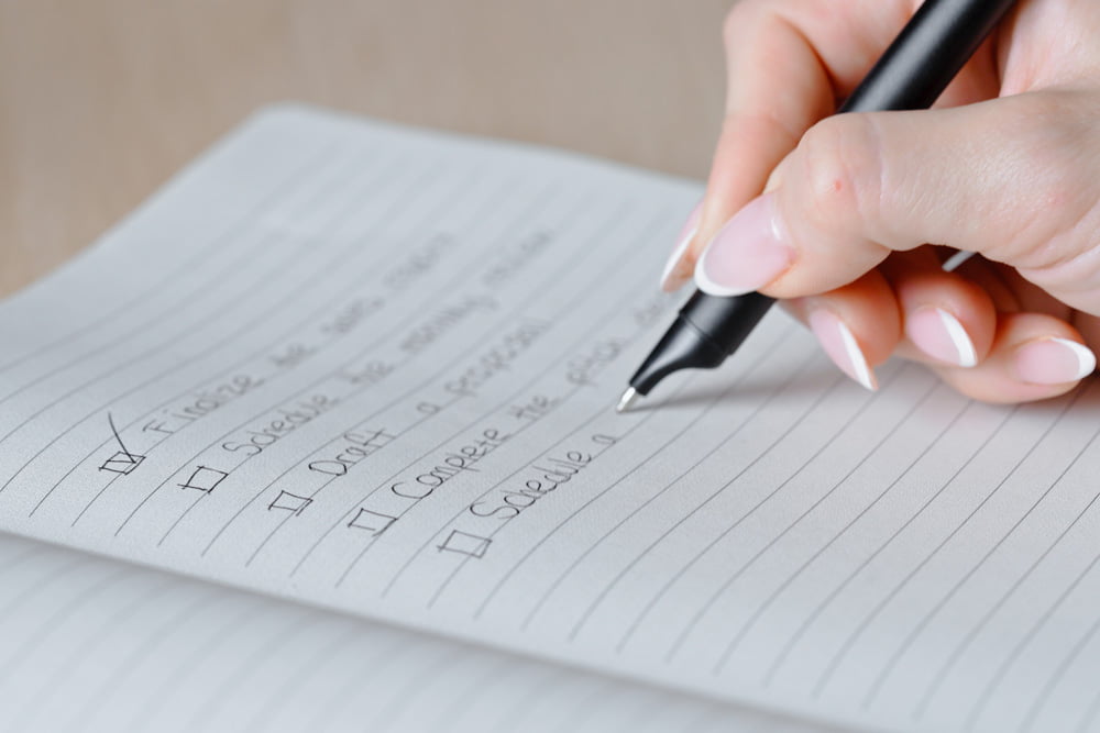 Close-up of a hand writing checkmarks in a lined notebook