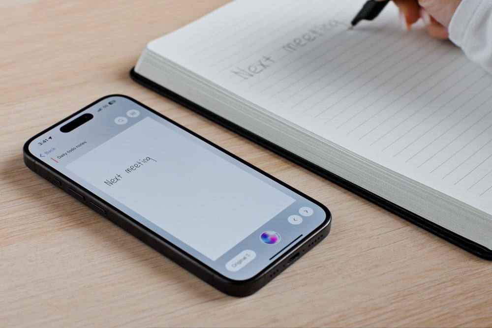 Writing 'Next meeting' in notebook beside smartphone with XNote